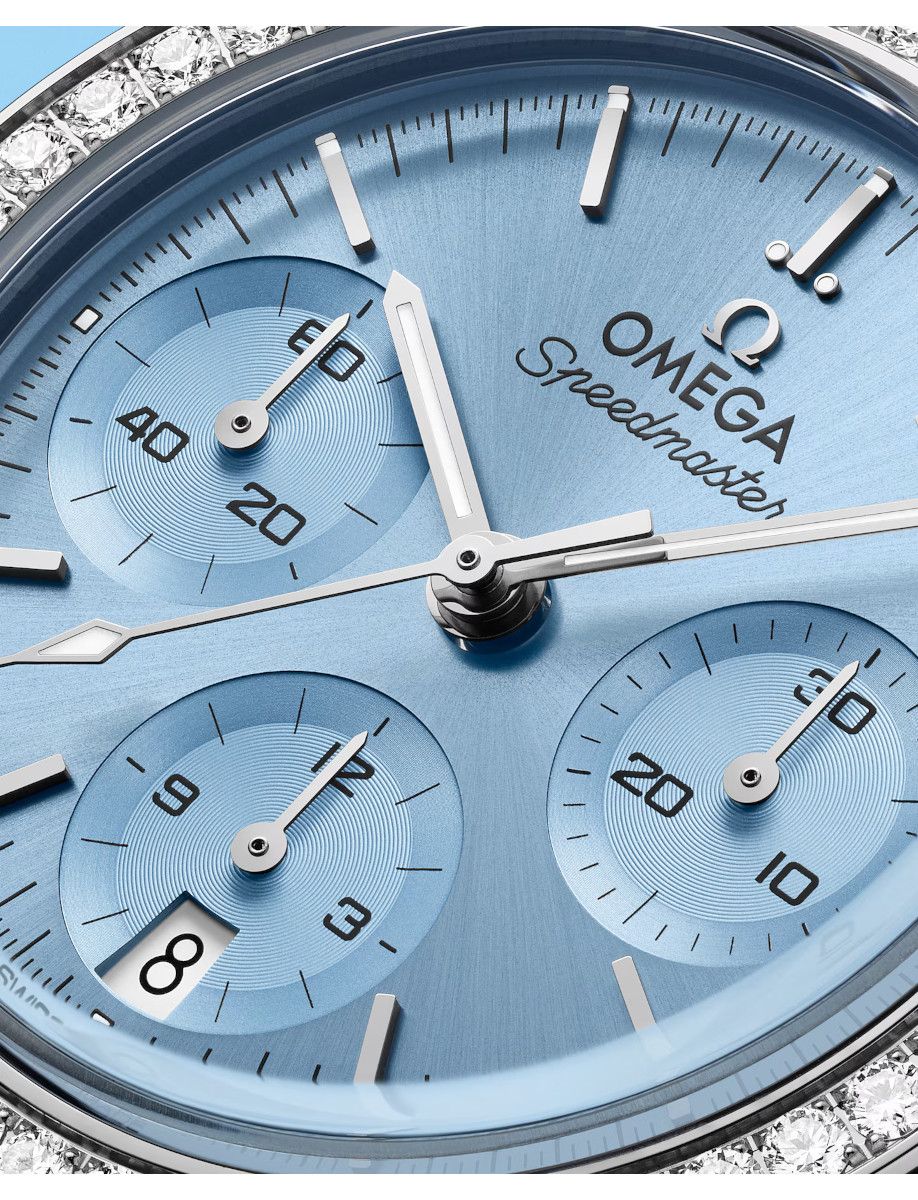 Close-up of a blue Omega Speedmaster watch face with three chronograph subdials and a diamond-studded bezel, showing silver hands and markers.