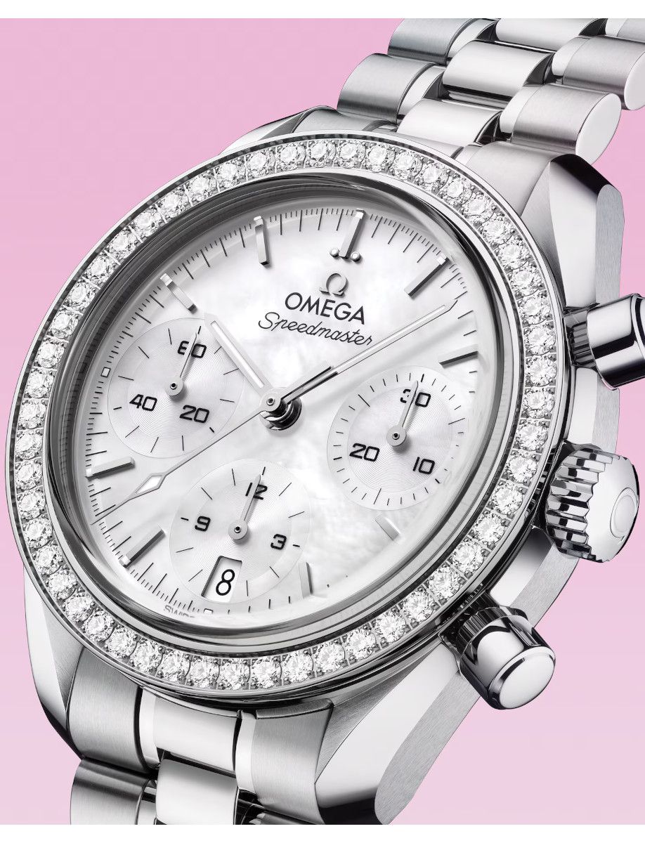 Omega Speedmaster stainless steel chronograph watch with a diamond-stud bezel and white dial on a pink background.