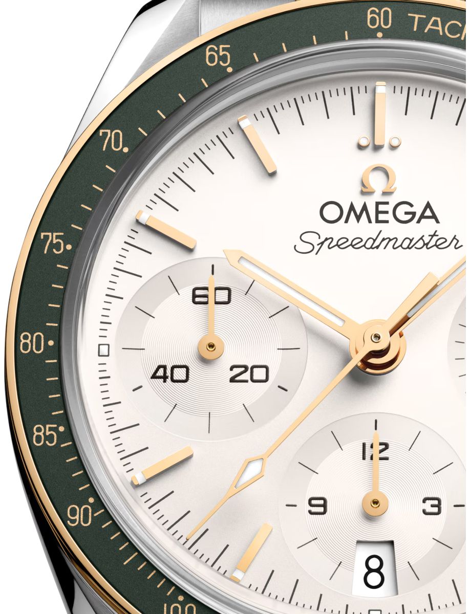 Close-up of an Omega Speedmaster watch face: white dial with gold hands and markers, three subdials, and a dark green tachymeter bezel with gold numerals.