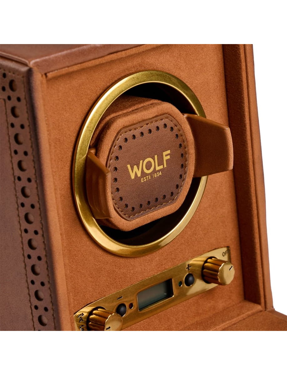 Close-up of a brown leather-wrapped Wolf control dial inside a gold-ringed circular opening on a caramel-colored cabinet, with brass knobs nearby.