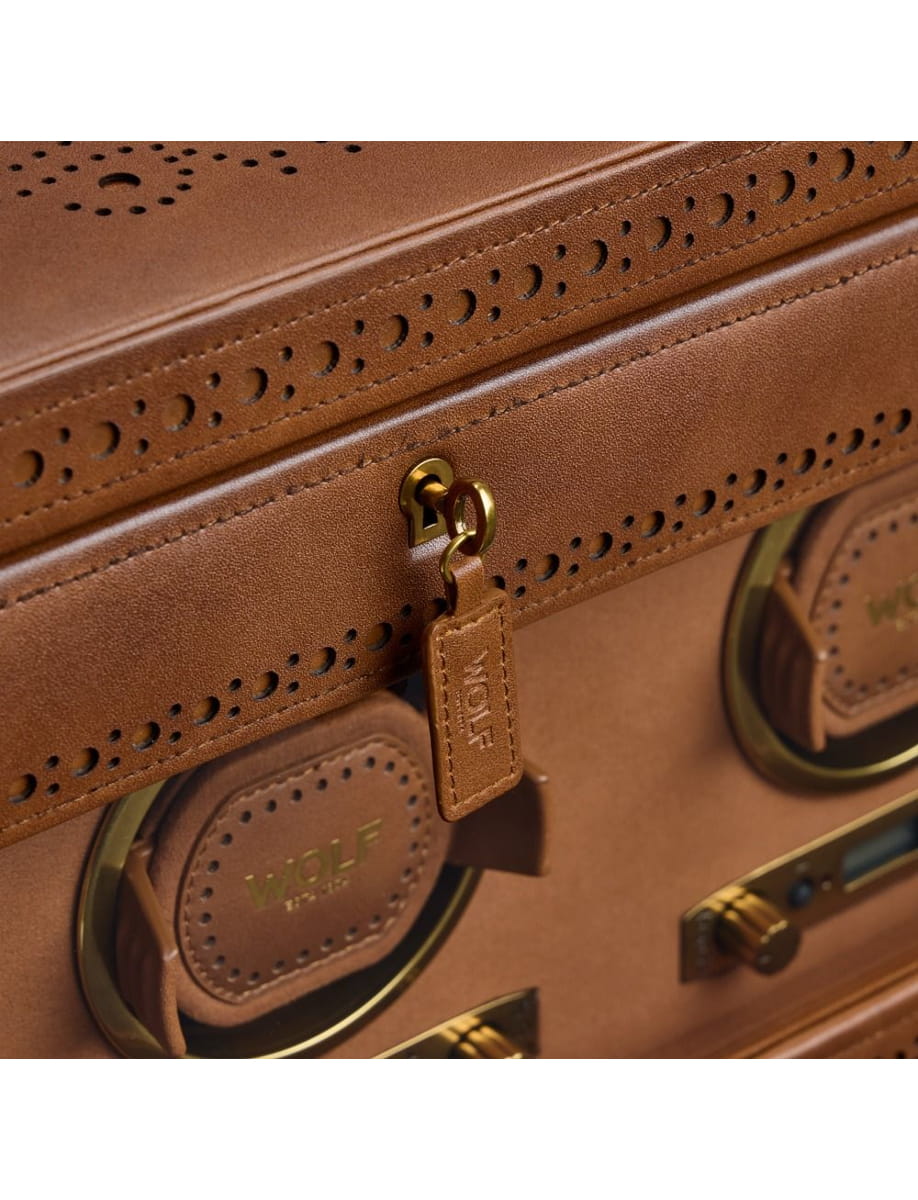 Close-up of brown leather luggage with brass hardware, a zipper pull, perforated trim, and rounded badge patches reading 'WOLF' near the handles.