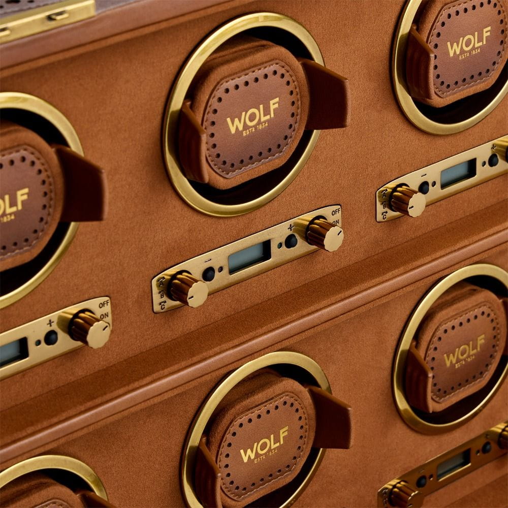 Close-up of brown leather-wrapped circular hardware on a Wolf storage case with brass rings and dials labeled EST 1834