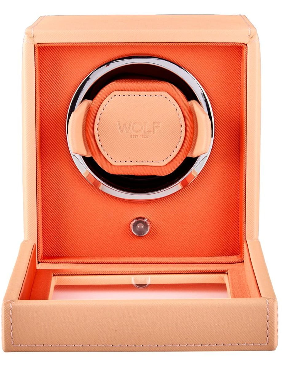 Peach leather watch winder box opened to reveal an orange interior and circular chrome wind rotor labeled Wolf.