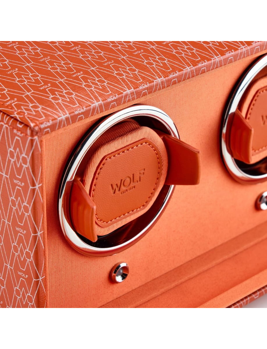 Close-up of an orange suitcase showing a circular chrome wheel housing and a leather pull tab embossed with WOLF