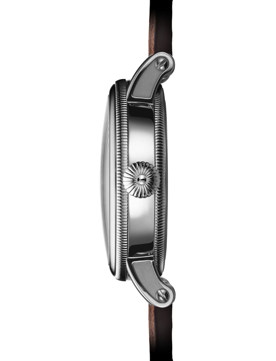 Close-up side view of a steel wristwatch with a textured crown and brown leather strap.
