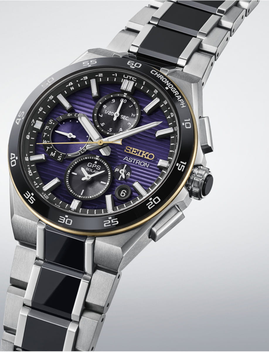 Close-up of a Seiko Astron titanium chronograph wristwatch with purple striped dial, multiple subdials, and a silver/black titanium bracelet.