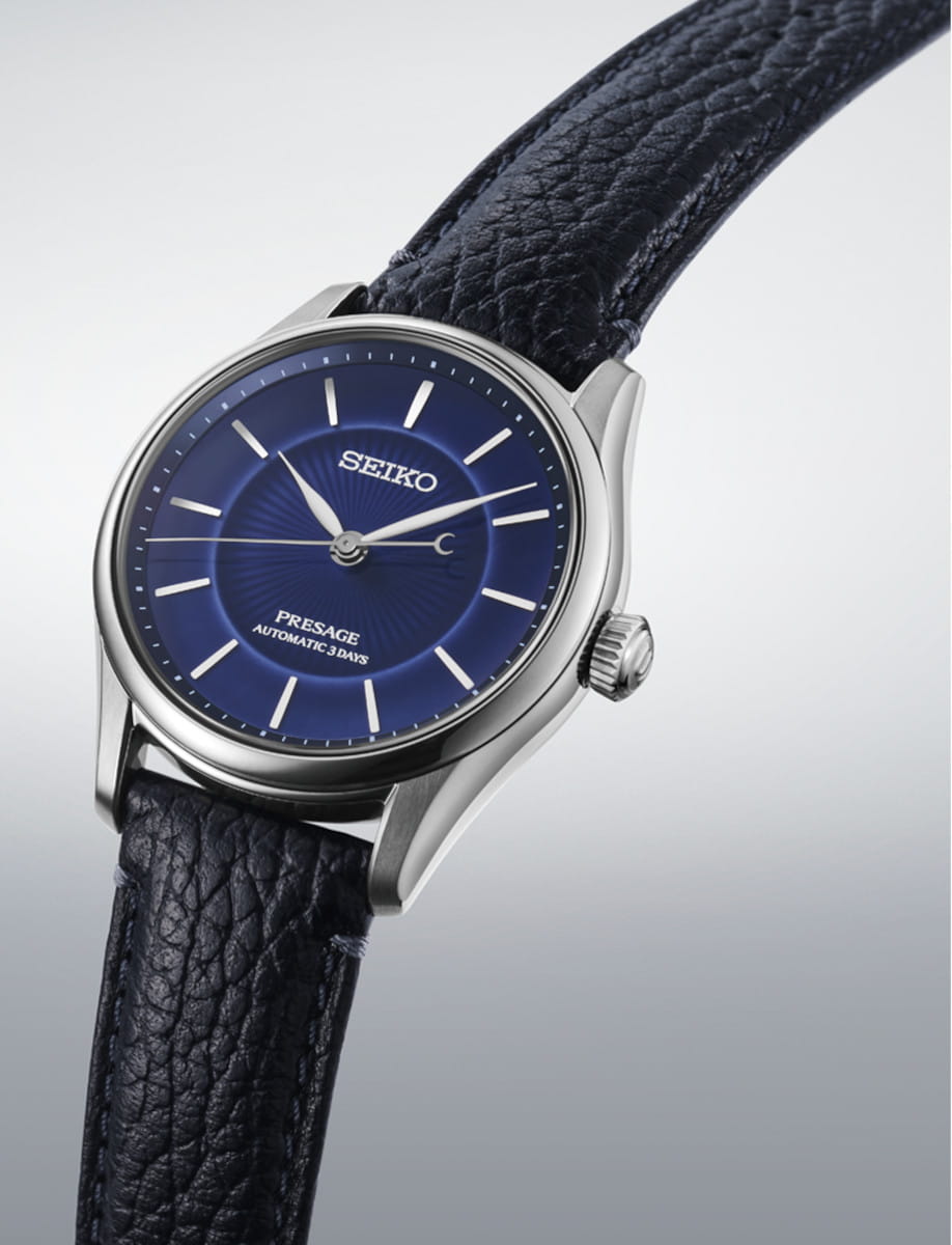 Close-up of a Seiko Presage automatic watch with a blue dial and black leather strap, angled on a gradient background.