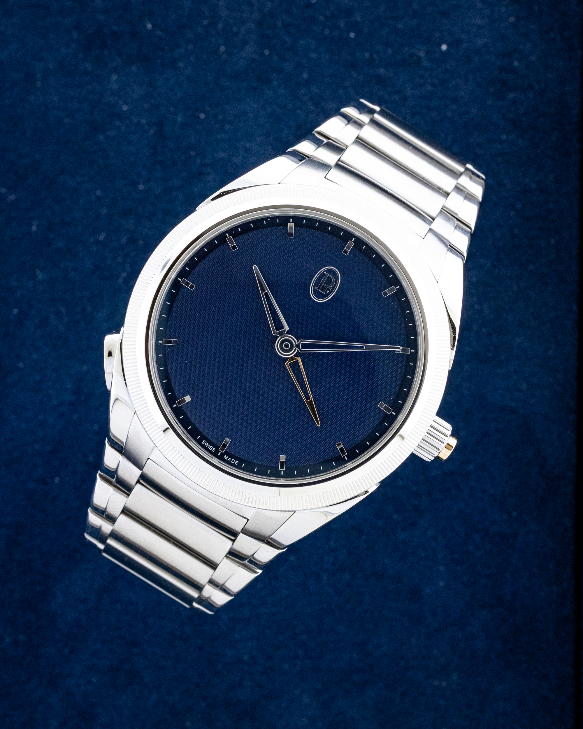 Close-up of a silver stainless steel wristwatch with a deep blue dial on a dark blue background.