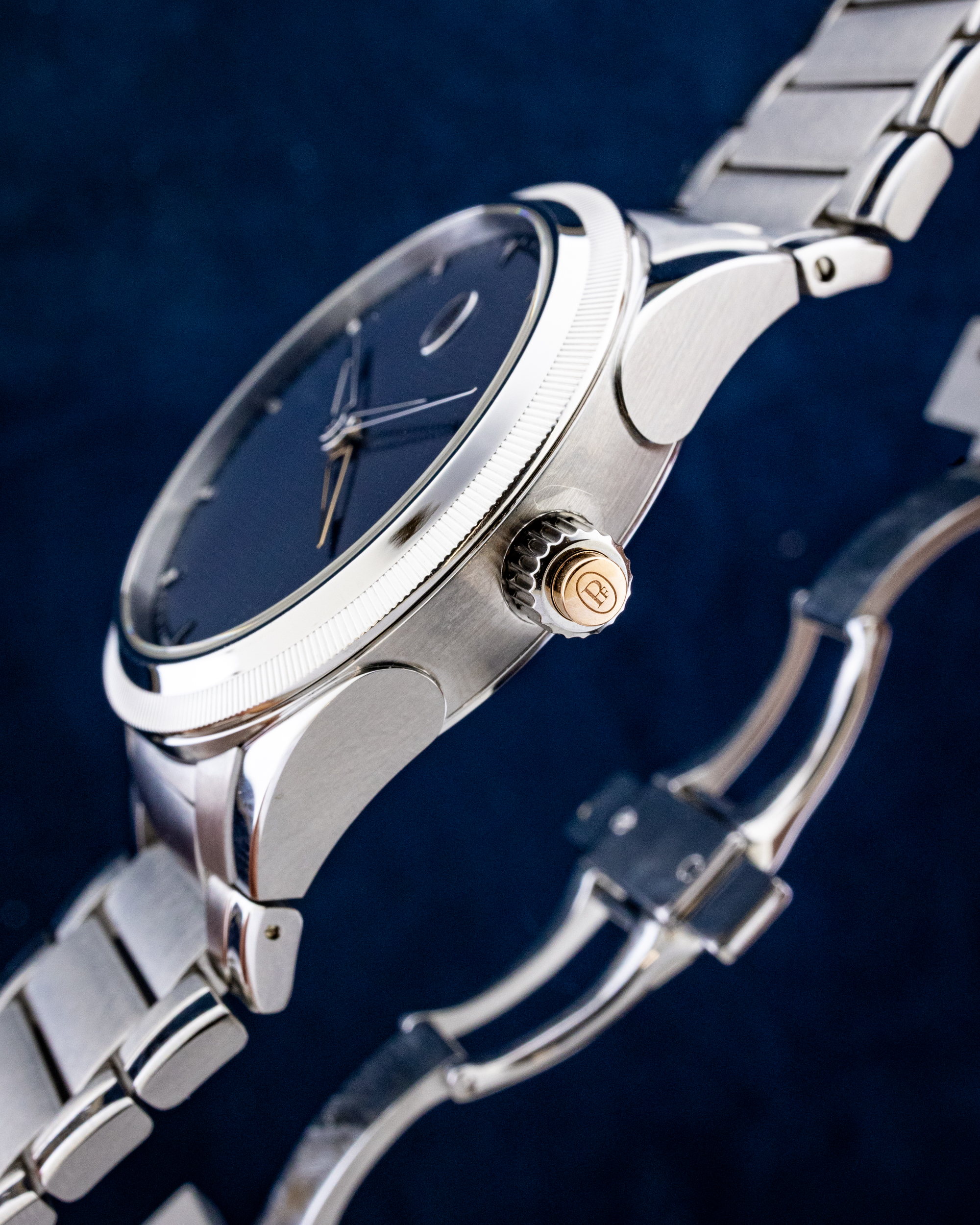 Close-up of a silver wristwatch with a dark dial and gold crown against a blue background