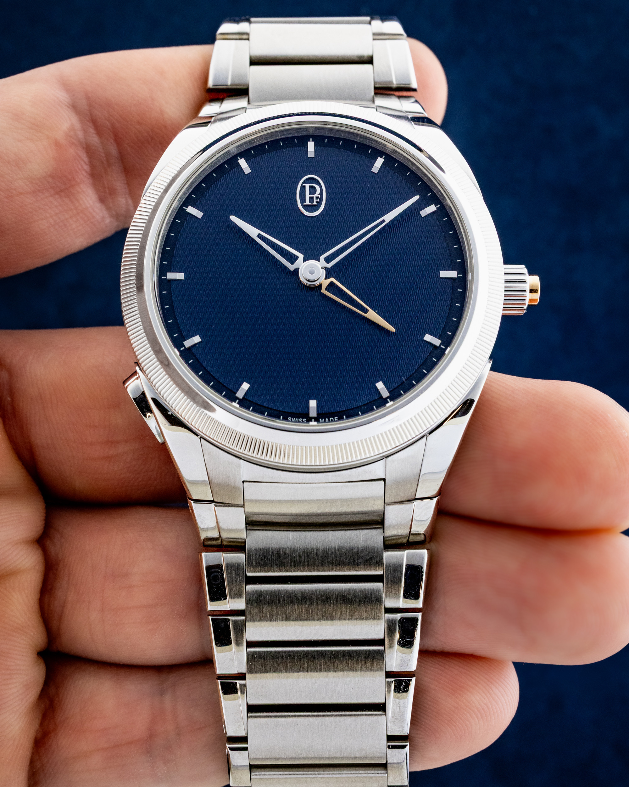 Close-up of a silver wristwatch with a blue dial being held by a hand, showing a metal bracelet and crown.