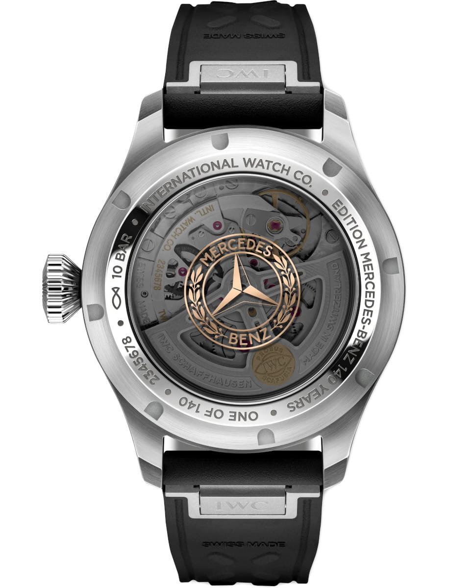 Back view of a silver IWC watch with a transparent case showing inner mechanics and a gold Mercedes‑Benz crest surrounded by laurel, attached to a black rubber strap
