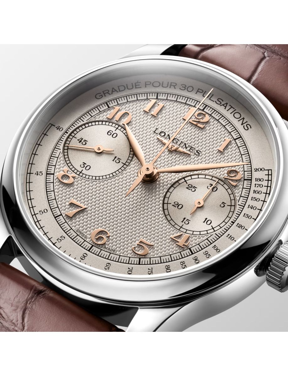 Close-up of a silver Longines chronograph watch with rose-gold numerals, two subdials, and a brown leather strap.