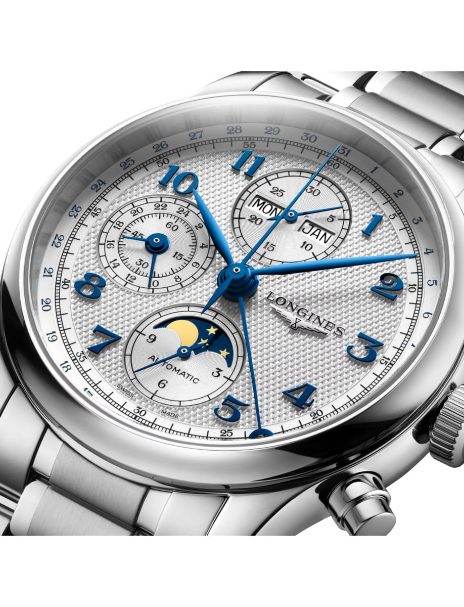 Close-up of a silver Longines wristwatch with blue hands and multiple subdials, including moon phase indicator and date window on a textured dial.