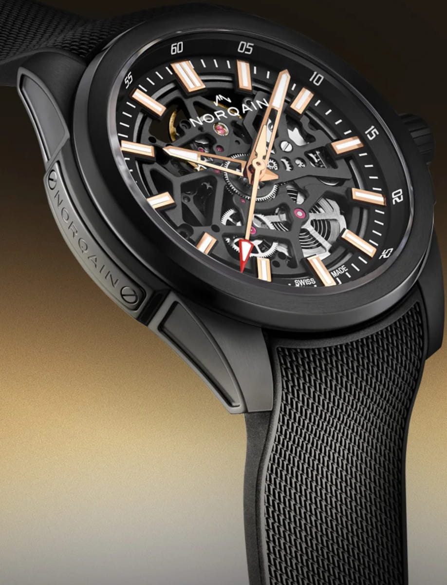 Close-up of a black skeleton wristwatch showing exposed gears, orange hands, and a textured strap.