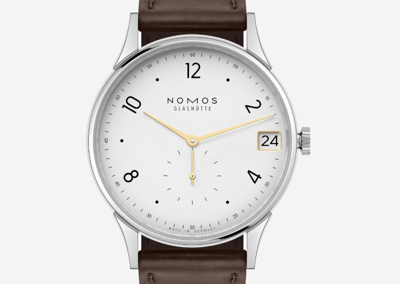 NOMOS Glashütte wristwatch with white dial, gold hands, stainless steel case and brown leather strap, date window showing 24.