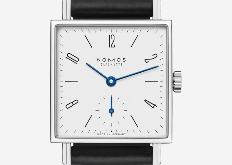 Nomos Glashütte wristwatch with a square silver case, white dial, blue hands, and a black leather strap.