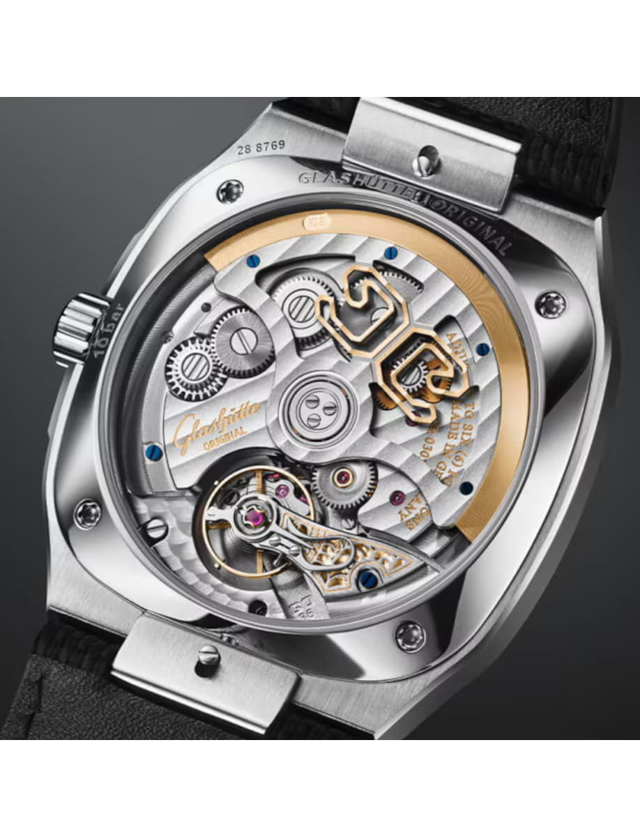 Close-up of a luxury mechanical watch movement, showing gears, a gold rotor, blue screws, and polished metal plates from the case back view