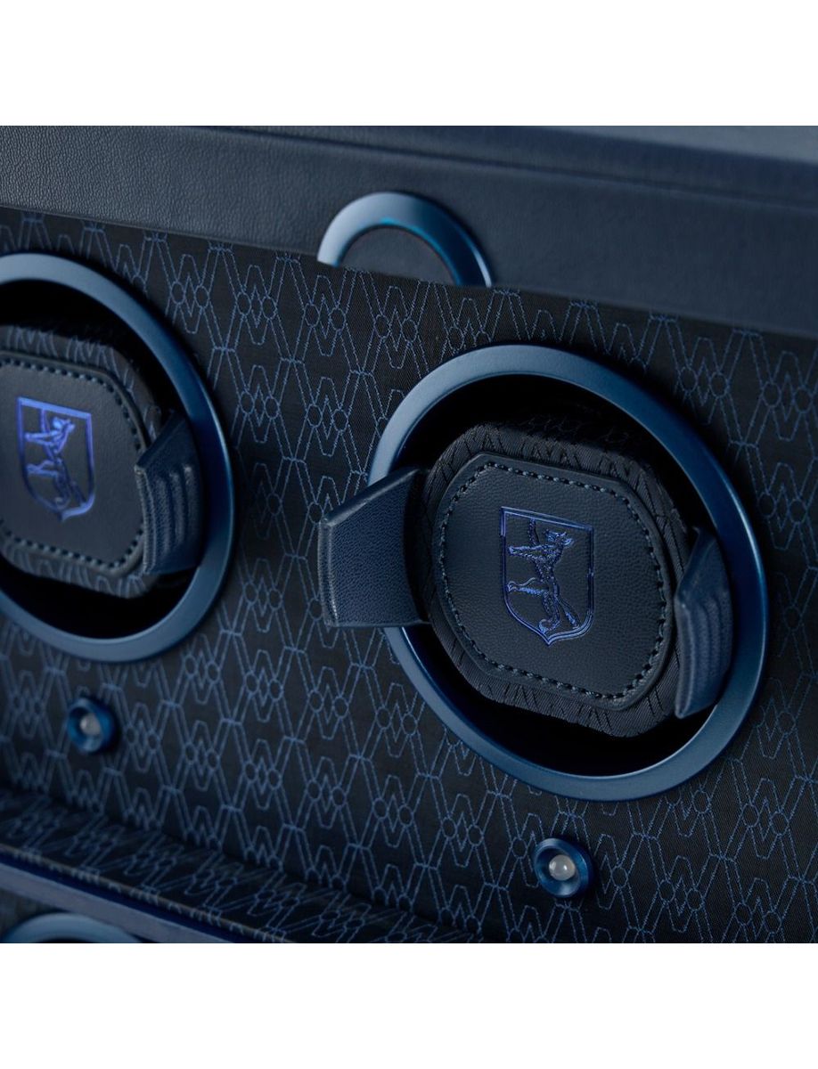 Close-up of blue over-ear headphones with stitched leather pads resting in a patterned blue speaker enclosure.