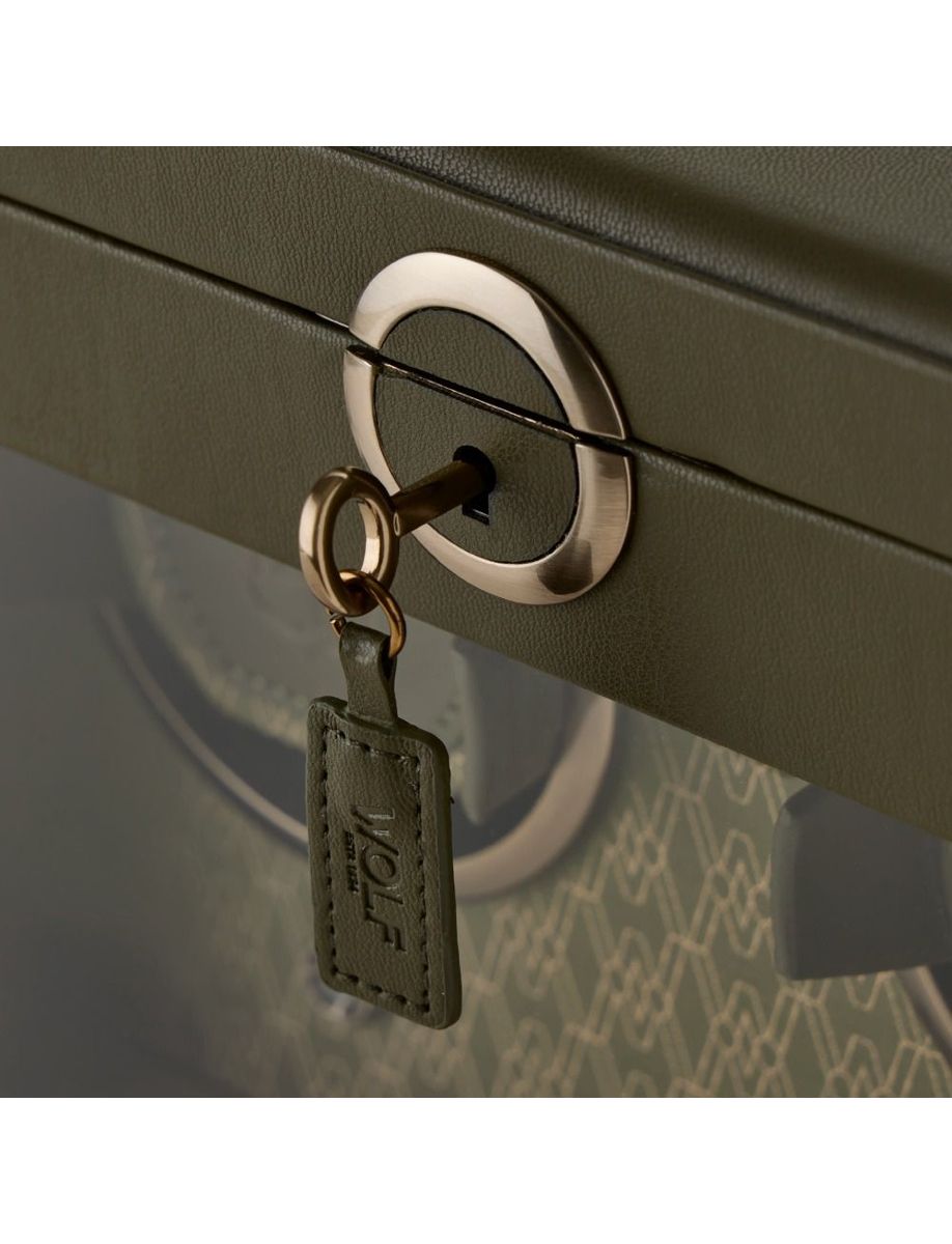 Close-up of a key inserted into a round luggage lock on a green suitcase, with a leather key tag hanging from the key rim.