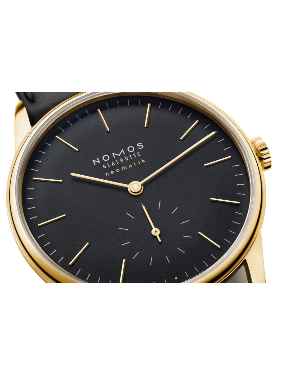 Close-up of a gold NOMOS Glashütte neomatik wristwatch with a black dial and minimalist gold indices and hands