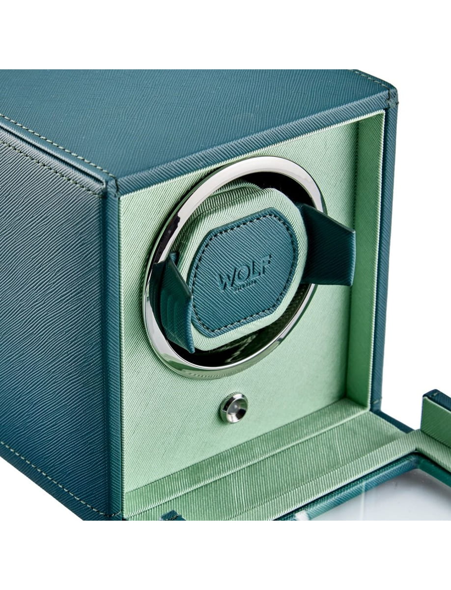 Open jewelry presentation box with teal interior, showing a round metal ring holder and a teal cushion labeled 'WOLF' inside.