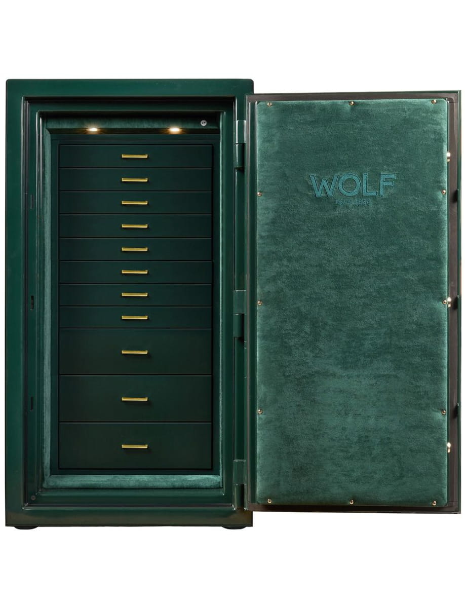 Open green Wolf-brand safe with multiple shallow drawers and gold handles, interior lit by two small lights above the drawers.
