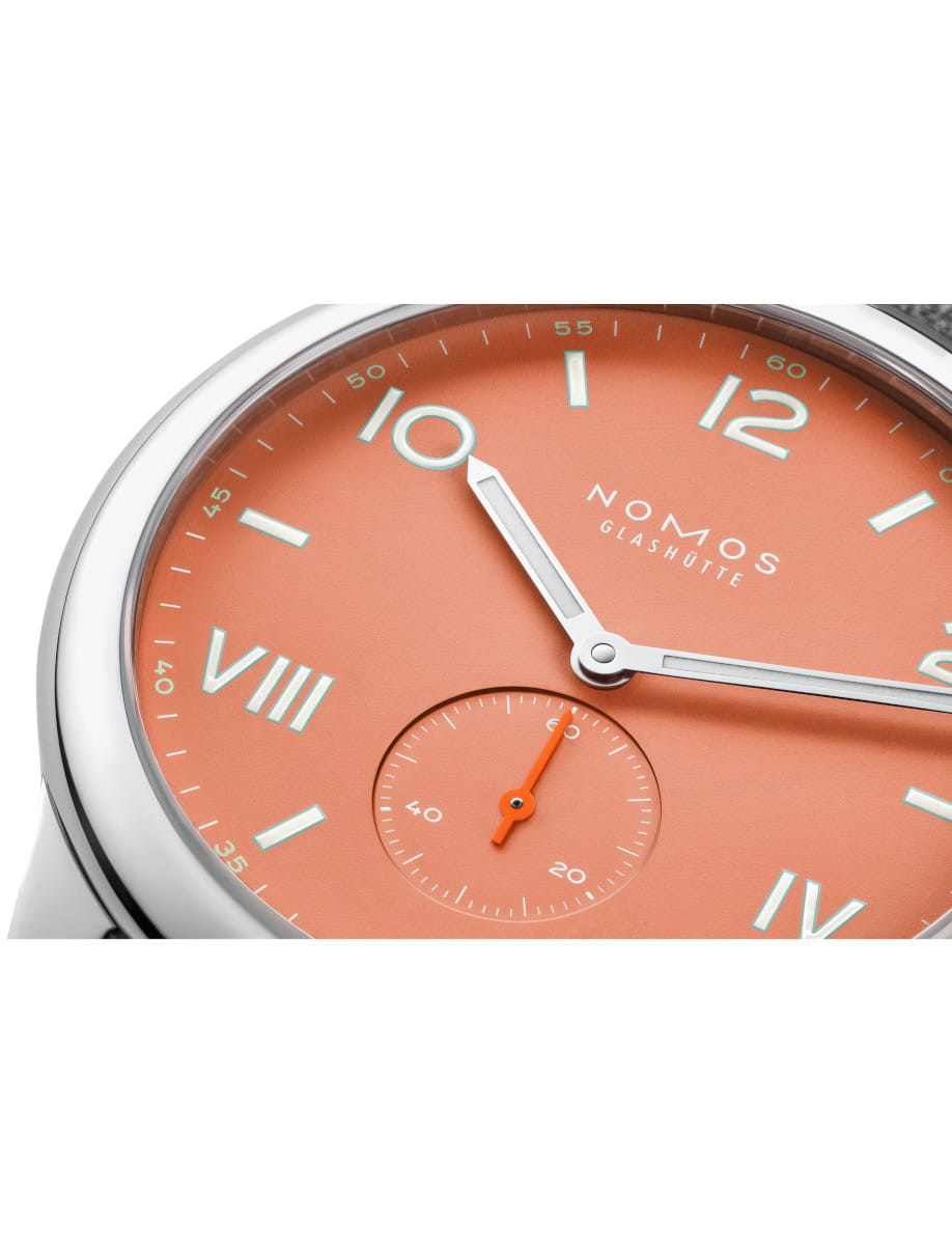 Close-up of a coral dial Nomos Glashütte wristwatch with silver hands and a small seconds subdial with an orange hand.