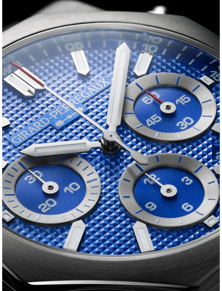 Close-up of a blue textured dial luxury watch with three silver subdials and bold white hands, displaying the brand Girard-Perregaux.