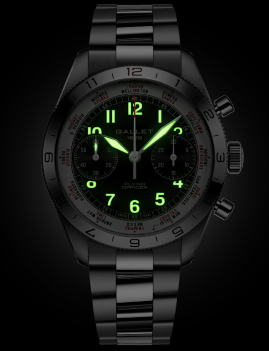 Luminescent green numbers and hands glow on a dark wristwatch face, stainless steel band.