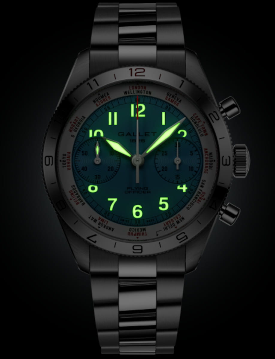 Stainless steel wristwatch with a teal dial, glowing neon-green numerals and hands, two subdials, and a rotating bezel against a dark background.