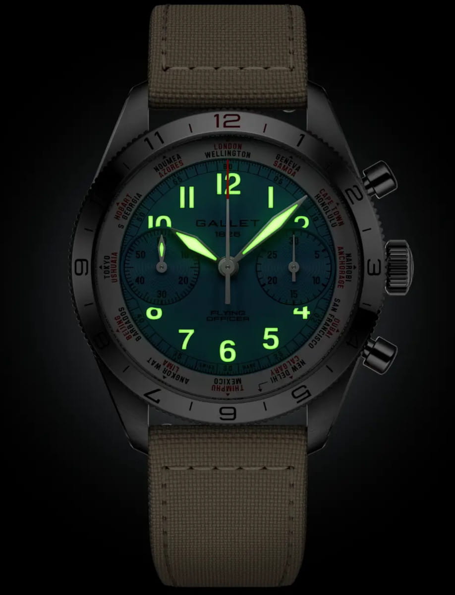 Gellet wristwatch with glowing green numerals on a blue dial, beige fabric strap, and multiple subdials against a dark background.