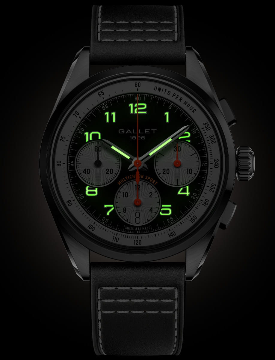 Black chronograph wristwatch with glowing green numerals on a dark dial and leather strap, showing subdials and a tachymeter bezel.