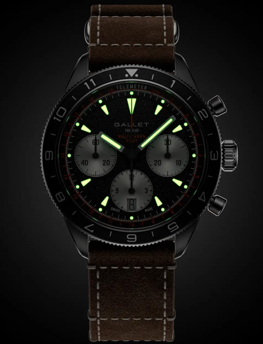 Black chronograph wristwatch with glowing green hands and hour markers, brown leather strap.