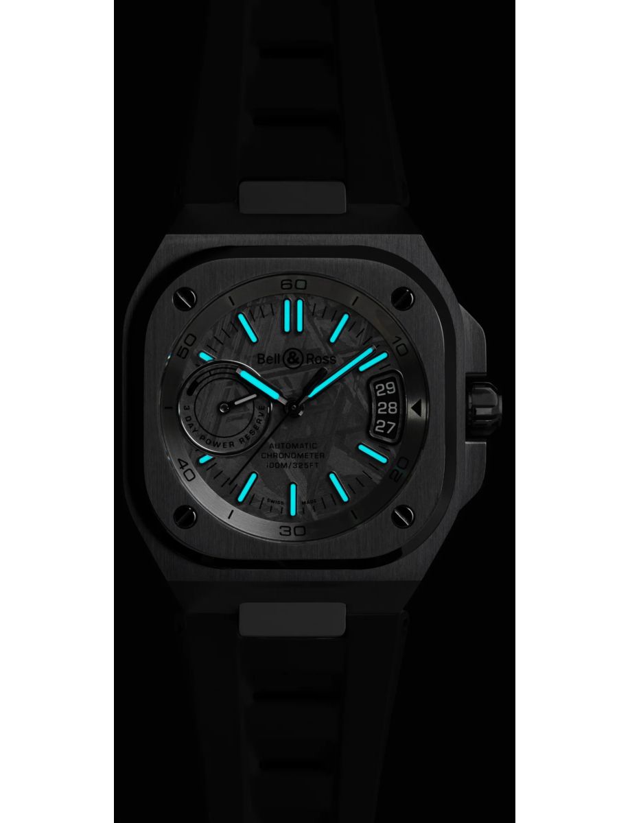 Bell & Ross wristwatch with glowing blue markers and hands on a dark dial, date window on the right edge, black strap behind it