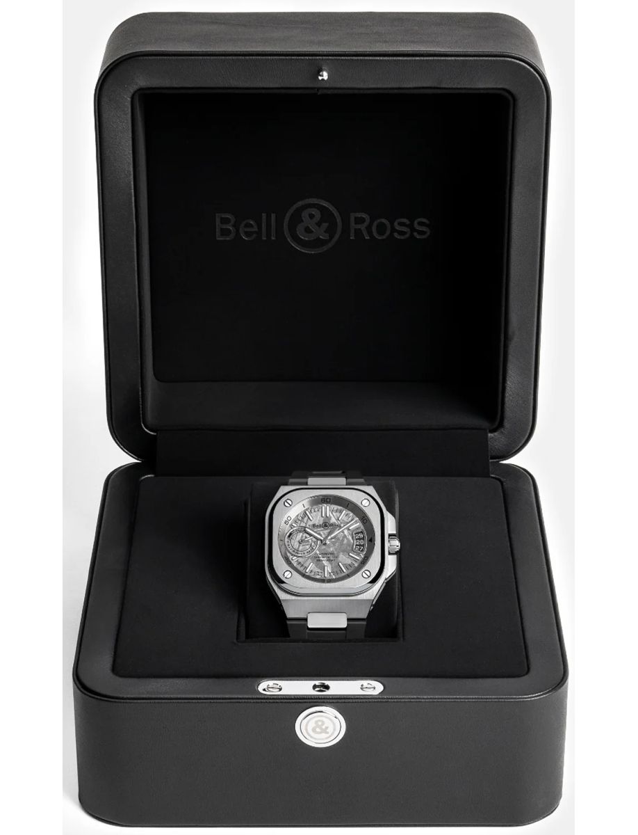 Bell & Ross wristwatch in a black presentation box, silver case with a skeleton dial showing gears and screws.