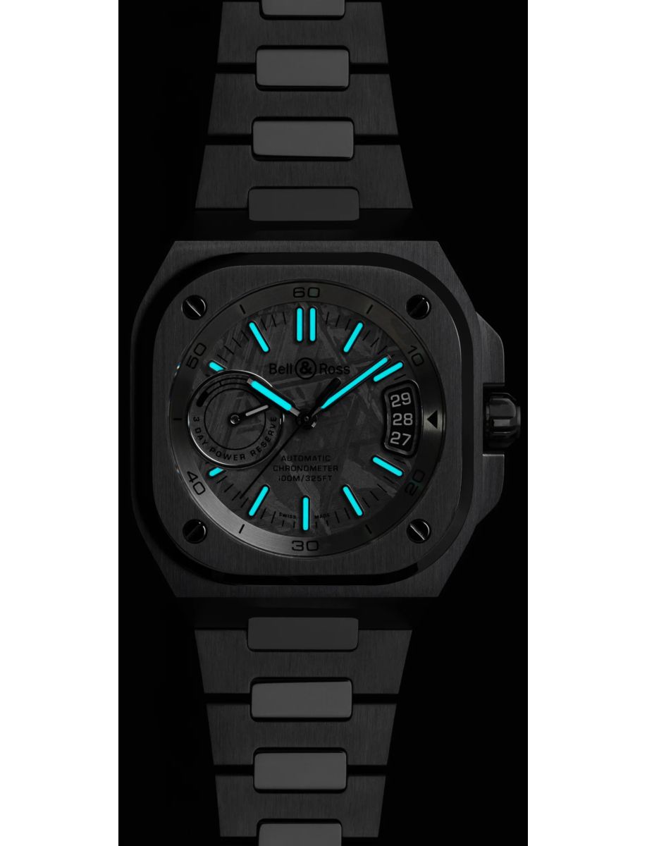 Bell & Ross steel watch with glowing blue hour markers and black dial, date window at 3 o'clock, metal bracelet on black background