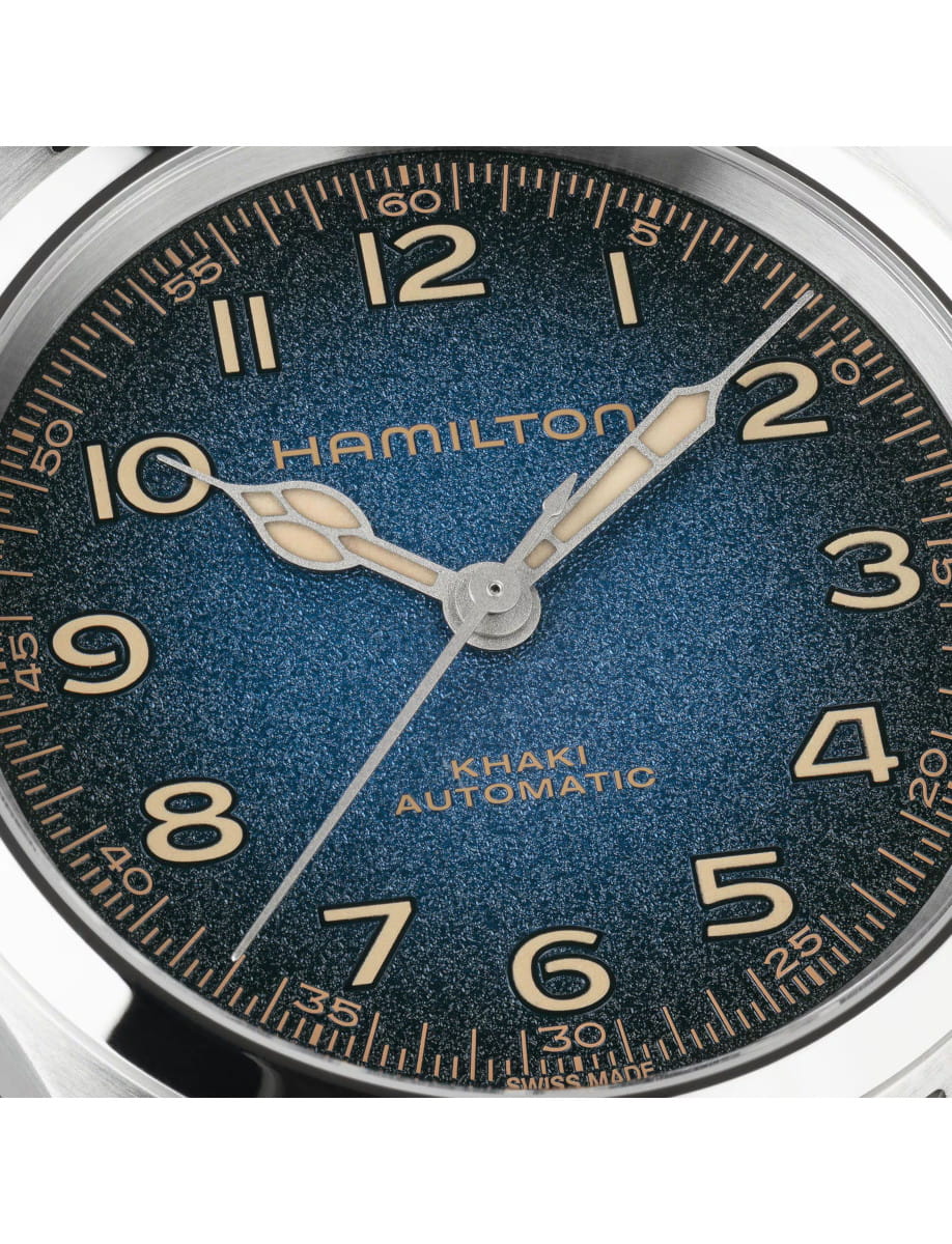 Close-up of a blue dial Hamilton Khaki Automatic wristwatch with large Super-LumiNova numerals and luminous hands, showing 'HAMILTON' branding.