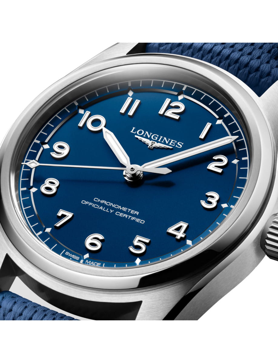 Close-up of a Longines wristwatch with a blue dial, white numerals, and a blue fabric strap.