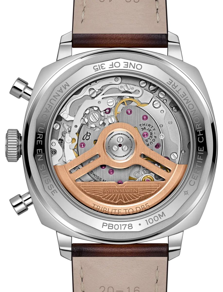 Back view of a polished metal Aston Martin wristwatch showing its intricate mechanical movement through a transparent case, with a copper rotor and engraved details.