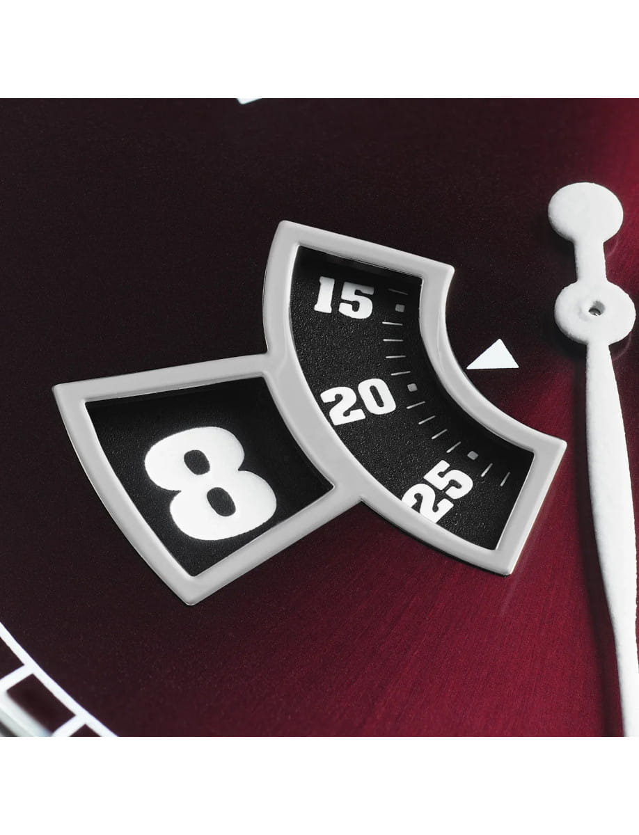 Close-up of a Bremont watch with a burgundy dial, hour and minute windows.