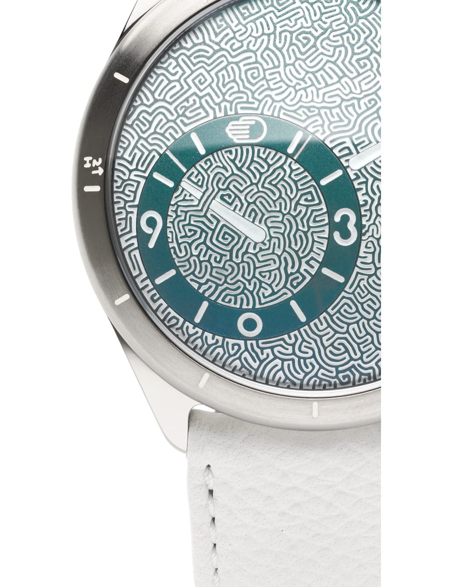 Close-up of a modern wristwatch with a labyrinth-pattern dial, and white strap, showing intricate maze details.