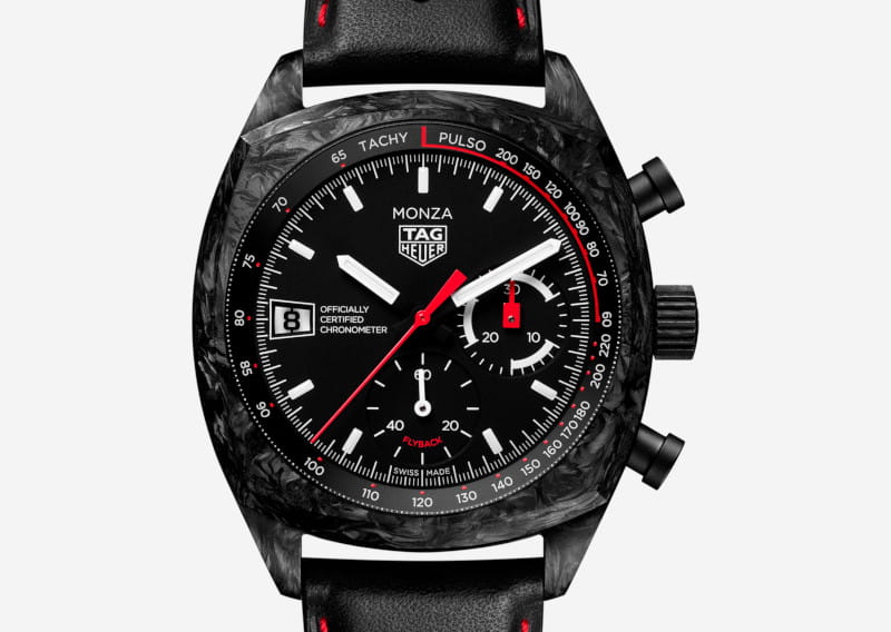 Monza TAG Heuer chronograph watch with a black face, white markers, red second hand, date window at 9 o'clock, and a textured black case with a black leather strap.