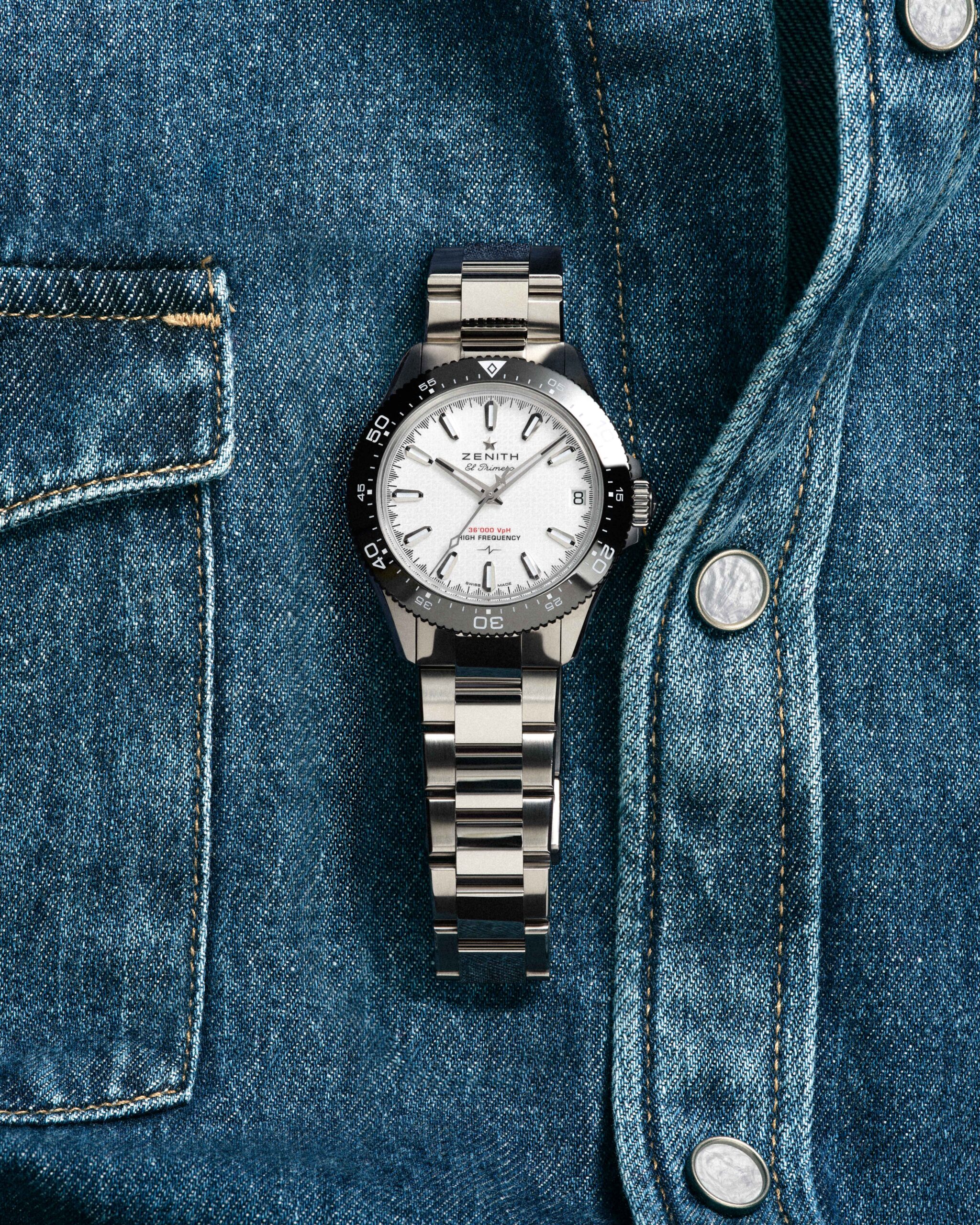 Close-up of a stainless steel wristwatch tucked into a blue denim jacket pocket.