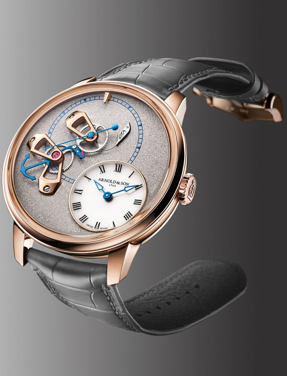 Red gold Arnold & Son wristwatch with an open-worked dial, blue hands, exposed gears, and a grey leather strap.