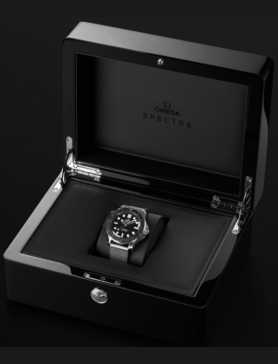 Omega Spectre wristwatch in a black open display box with a metal mesh band and black dial, centered on a padded tray.