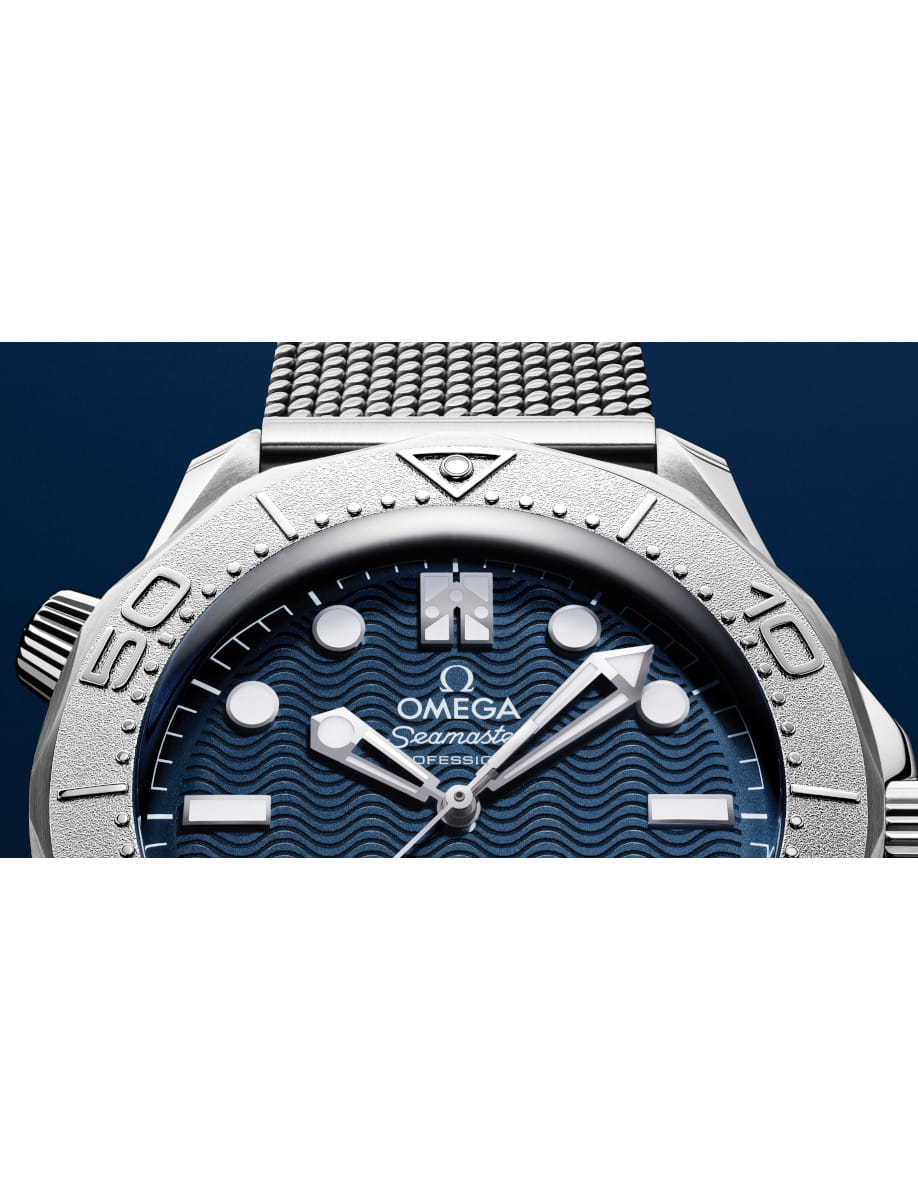 Close-up of an Omega Seamaster Professional watch face with a blue dial, bold indices, and a mesh bracelet visible at the top edge.