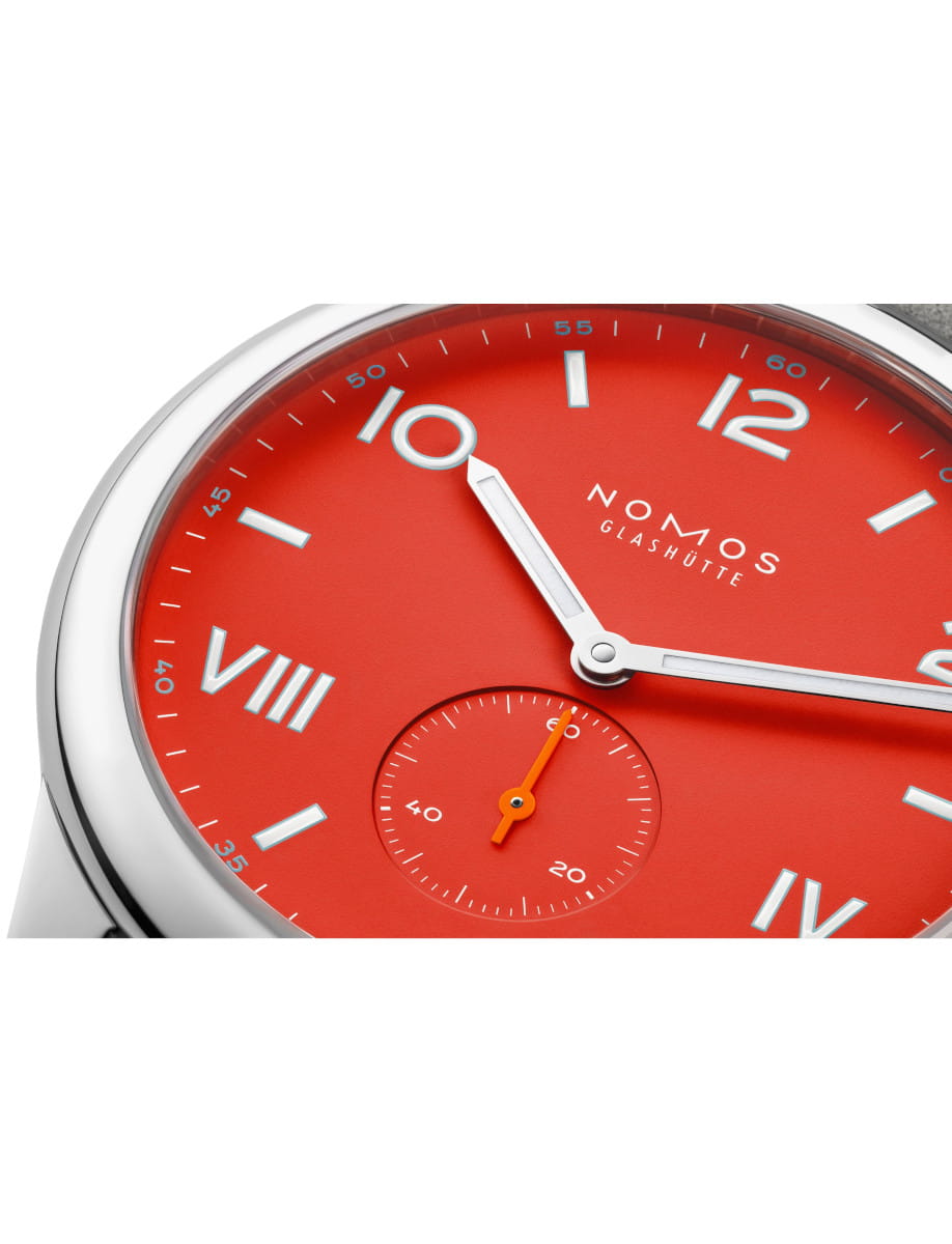 Close-up of a red NOMOS Glashütte wristwatch face with silver hands and a small seconds subdial.