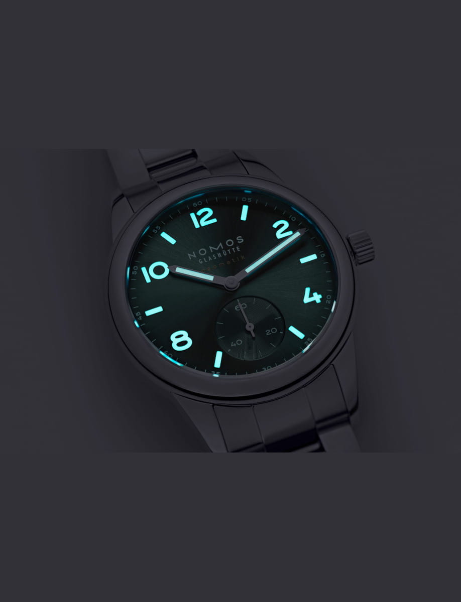 NOMOS Glashütte wristwatch with stainless steel case and bracelet, and petrol green dial and luminous hands and hour markers.
