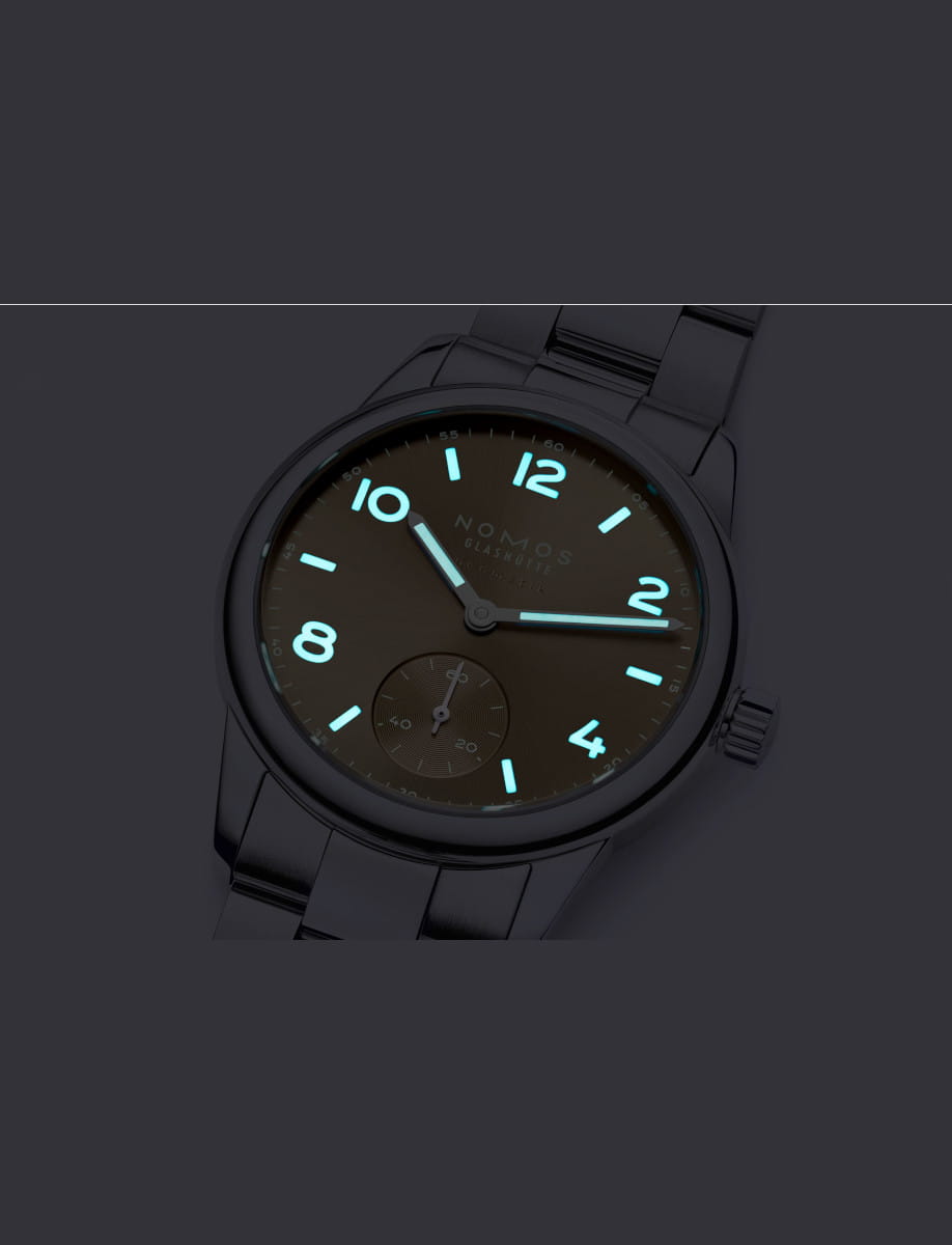 NOMOS Glashütte wristwatch with stainless steel case and bracelet, and gold dial with luminous hands and hour numerals.