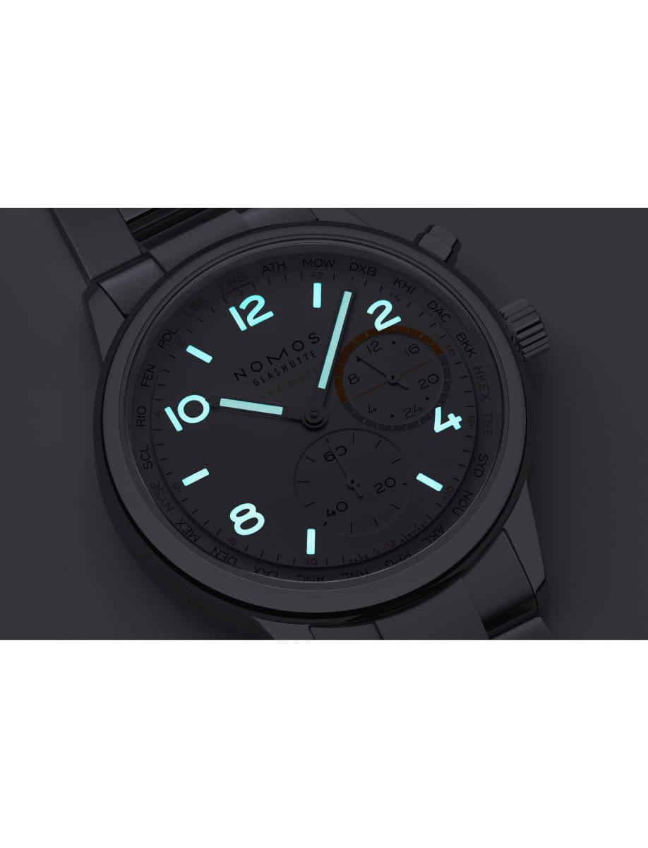 Dark wristwatch with glowing blue numerals and hands, Nomos Glashütte branding visible on the dial.